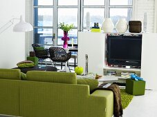 Green sofa and half height white entertainment center with flower vases in front of patio doors