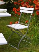 White folding chair in a garden with red flowers