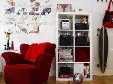 Red upholstered chair and white shelves and a skateboard on the wall