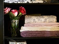 Quilted and embroidered wool blankets next to a bouquet of roses in a black cabinet