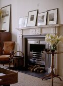 A detail of a traditional sitting room, showing carved fireplace with black hearth, wooden round side table