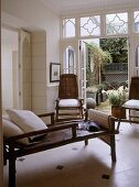 A modern country sitting room with French doors opening out on to garden, bamboo cane day bed, chairs, tiled floor