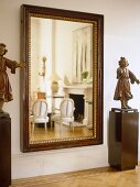 Statues on plinths either side of mirror reflecting sitting room