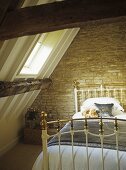 Brass bed with teddy bears under a pitched attic roof and skylight.