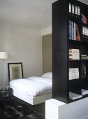 A single bed behind a partition of book shelves