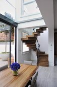 Vase of blue flowers on wooden table and chairs in contemporary open plan dining room with wooden staircase