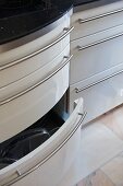 Weiß glänzende Schrankfronten teilweise geschwungen mit geöffneter Schublade in moderner Küche