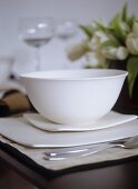 Close up of white ceramic bowl on modern square dishes, place mat, cutlery, flowers, wine glasses,, Interiors, dining, detail, tableware, modern, simple, elegant, stylish,