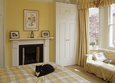 Cat sitting on bed with checked cover in yellow bedroom