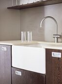 A detail of a modern kitchen, wooden units, a Belfast sink, chrome tap, glasses on draining board,