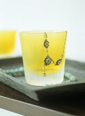 A detail of a yellow glass with jewellery set on a wooden tray,