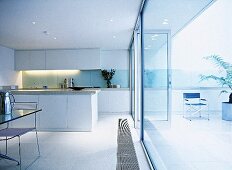 Modern kitchen and dining area with white cabinets, glass backsplash, wall of windows, and a tiled floor.