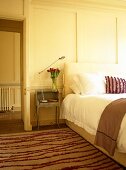 Bedroom with pink striped rug and cushion and white panelled walls.