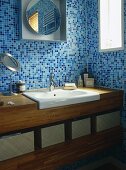 Waschtisch aus Holz und moderner Spiegel vor blauen Mosaikfliesen in Badezimmerecke