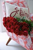 Rote Rosen und Kissen mit Liebesgruss auf Sessel