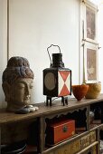 Antikes Sideboard mit Buddhakopf neben alter Laterne