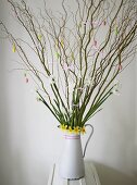 Budding branches and spring flowers with Easter decoration in a white pitcher