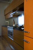 Küche mit Holzschrankfront und orangem Kühlschrank