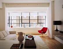 An open-plan, modern living room with a mixture of styles - a light-coloured sofa and a red armchair