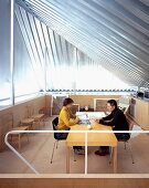 A couple sitting at a table in an open attic room with metal panelling