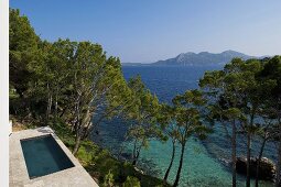 A pool with a stone terrace on a hillside in a Mediterranean landscape and a sea view