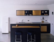 A modern, open-plan kitchen with a bar and cupboard with black frames and wooden fronts