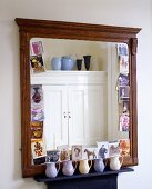 A mirror with an antique wooden frame and a collection of jugs on the shelf below