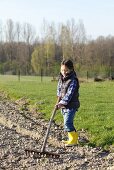 A little girl in a garden with a rake