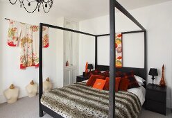 Decorative cushions and a quilt on a bed on a four poster bed and a kimono hanging on the wall in a bedroom