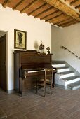 A piano next to a flight of steps in an entrance hall with a terracotta floor