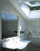 Curved designer sink with a recessed mirror in the wall and open skylight window