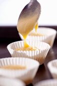 Dough being poured into paper cases from a spoon