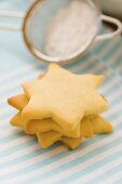 Four star-shaped biscuits in a pile with icing sugar