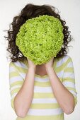 Woman holding a lettuce in front of her face