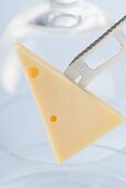 Stück Emmentaler auf Spitze eines Käsemessers vor Käseglocke