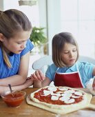 Two girls putting mozzarella on top of a pizza