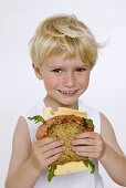 Blond boy holding salami and cheese sandwich in his hands