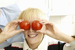 Blond boy holding two tomatoes in front of his eyes