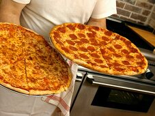 A Man Holding Two Fresh Baked Pizzas