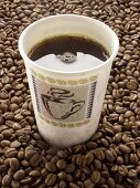 Black Coffee in a Paper Cup Resting On Coffee Beans