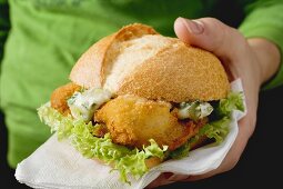 Hand holding fish burger with remoulade sauce
