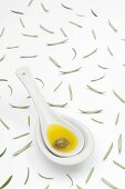 A spoon of olive oil and an olive and scattered rosemary leaves