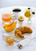 Frühstück mit Melone, Croissant, Ei, Marmelade, Kaffee und Orangensaft