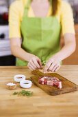 Woman Adding Fresh Herbs to Season a Steak