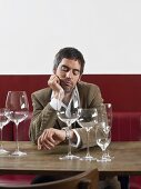 A man sitting at a table with empty wine glasses looking at his watch
