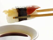 Sushi on chopsticks above soy sauce