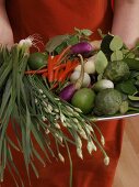 Woman holding plate of Asian vegetables, herbs etc