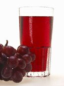 Glas roter Traubensaft und rote Trauben mit Wassertropfen
