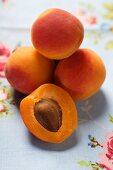 Aprikosen, eine halbiert, auf geblümtem Tischtuch