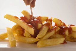 Hand nimmt Pommes frites mit Ketchup auf Spiesschen